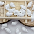 Detailed view of white shell-shaped ceramic beads for DIY jewelry on a wooden tray - White