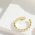 Detail eines verstellbaren Goldrings mit weißen Emaille-Herzen auf strukturiertem Gips - Weiß