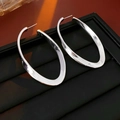 Close-up of oversized silver irregular oval hoop earrings on a black textured jewelry box - Silver