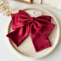 Detail einer großen weinroten Satin-Schleife Haarspange auf einem Steintablett - Weinrot