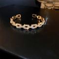 Macro shot of gold-plated chain bracelet with cubic zirconia detailing on black surface - Gold