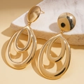 Detailed view of golden geometric drop earrings resting on white marble stone - Gold