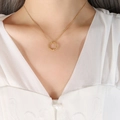 Golden twisted circle pendant necklace on female model wearing white V-neck top - Gold Necklace