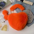 Detail of bright orange heart-shaped faux fur bag with gold chain and plush pom charms - Orange