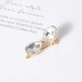 Elegant gold bow hair clip featuring two large teardrop crystal stones on white paper - White