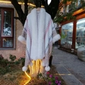 Close-up of knit poncho with faux rabbit fur trim and decorative pom-pom detailing - White Beige