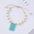 Detail of bohemian pearl bracelet featuring a light blue woven heart charm and gold beads - Light Blue Background Gold Heart