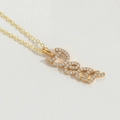 Detailed view of a gold Deed pendant necklace with sparkling pavé crystals on white leather - DEAR Letter