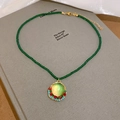 Dettaglio della collana di perline di cristallo con ciondolo in resina su un libro - Verde