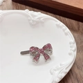 Close-up of a silver bow hair clip with pink rhinestones on a white ceramic plate - Bow / Pink