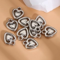 Pendentifs cœur en métal argenté Y2K pour bijoux DIY sur fond beige texturé - Double Cœur Creux
