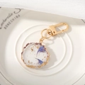 Detalle de un llavero artesanal de resina con flores secas moradas y toques de pan de oro - Pétalo Azul