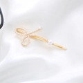 Elegant gold bow hair clip with white pearls on a soft white satin background - Bow