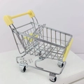 Close-up of mini metal shopping cart toy with silver wire mesh and yellow handle - Yellow