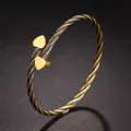 Detail eines gedrehten Titanstahl-Armreifs mit goldenen herzförmigen Anhängern - Herz-Stil / Glänzend