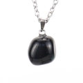 Detailed view of an irregular polished black stone pendant with a silver metal chain - Silver + Obsidian