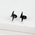 Macro detail of minimalist black lightning bolt stud earrings on a white stone base - 106 Lightning / Black