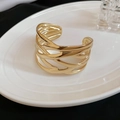 Detail van de goudkleurige open manchetarmband met geweven patroon op een wit bord - Gouden Hol Geweven / Goud