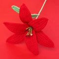Close-up of a handmade red crochet lily flower with green leaves on a matching red background - Finished Lily Stems - Red