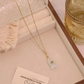 Detailaufnahme des goldenen Fisch-Anhängers mit weißem Naturstein und Zirkon auf Schmucktablett - Opal