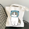 White canvas tote bag featuring a cute cat wearing a blue frog hat on a chair - Cat in Frog Hat