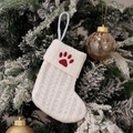 White knitted Christmas stocking with red paw embroidery hanging on a frosted pine branch - Embroidered Knitted Small Sock White Paw Print