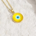 Golden necklace with bright yellow evil eye resin pendant on a textured stone surface - Yellow
