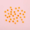 DIY flower-shaped orange glass beads scattered on pink background for jewelry making - Orange