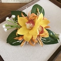 Nahaufnahme der gelben Orchideen-Haarspange mit grünen Blättern auf einem beigen Tablett - Gelb