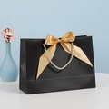 Elegant matte black gift bag featuring a large golden satin bow and braided rope handles - Black; Horizontal Extra Small Size 19*15*7 Ribbon Style