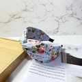 Blue fabric headband with pink floral pattern and twist design on a wooden desk - Blue Floral Print