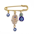 Golden Hamsa Hand brooch with sparkling rhinestones and blue Evil Eye charms on white background - Pin with Rhinestone Hamsa, Blue Eye, and Clear Bead