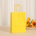 Detail of bright yellow kraft paper gift bag with matching twisted rope handles on a desk - Yellow