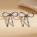 Detailed view of blue and white striped acetate bow earrings on a textured stone surface - Blue