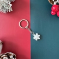 Silver metal keychain featuring a white snowflake pendant on festive red and green background - Snowflake