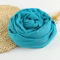 Bright blue cotton linen scarf with fringe edges folded into a rose shape on a straw mat - 190x100cm / Light Teal