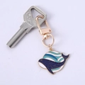 Enamel blue whale keychain with gold trim and glitter waves on white background - Blue Whale
