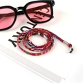 Detail of colorful bohemian braided eyewear cord with silver connectors on white background - US 10