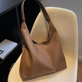 Bolso tote de cuero marrón con textura lichi y asa minimalista sobre silla blanca - Caqui