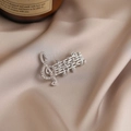 Silver musical note brooch with sparkling crystal pavé set on a beige silk fabric - 528 Notes