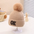 Detailed close-up of beige knitted beanie with fluffy fur pompom and black OK patch - One Size (2-5 Years) / Khaki