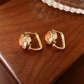 Close-up of golden letter M earrings with round cubic zirconia on dark wood texture - Gold M-Letter Round Ear Buckle