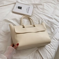 Cream colored faux leather tote bag with wavy flap design on white bed linens - White
