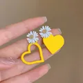 Detalle de pendientes asimétricos de margarita y corazón amarillos en una mano - 4# Pin de Acero - Amarillo - Margarita Corazón Asimétrico