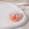 Detail of pink-orange carnation scented candle on white tray with champagne silk background - Orange