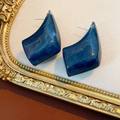 Dettaglio macro di orecchini in resina blu marmo su una cornice dorata vintage - Blu