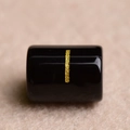 Close-up of black cylindrical bead with vertical gold stripe for DIY jewelry making - Letter I