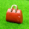 Colgante mini bolso de cuarzo rojo con asa de metal dorado sobre césped verde - Jaspe Rojo