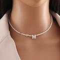White beaded necklace featuring a shell letter M pendant and small golden heart bead - M