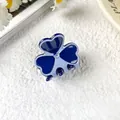 Blue clover-shaped acetate hair claw with central rhinestone on white plush background - Blue